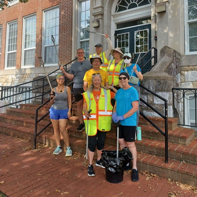 A cleanup crew in safety vests holding litter grabbers on the front steps of the library
